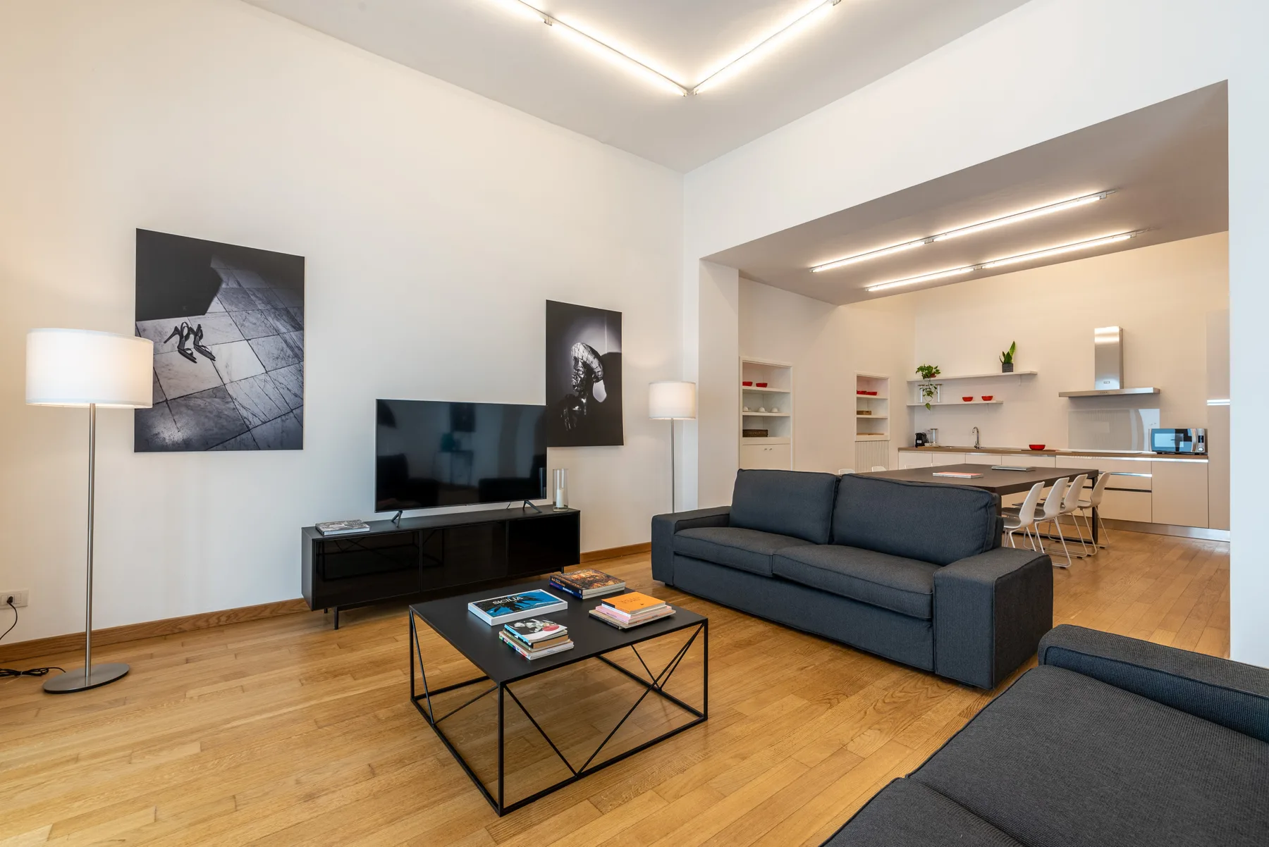 A modern living room with seating, a television, and an open kitchen beyond.