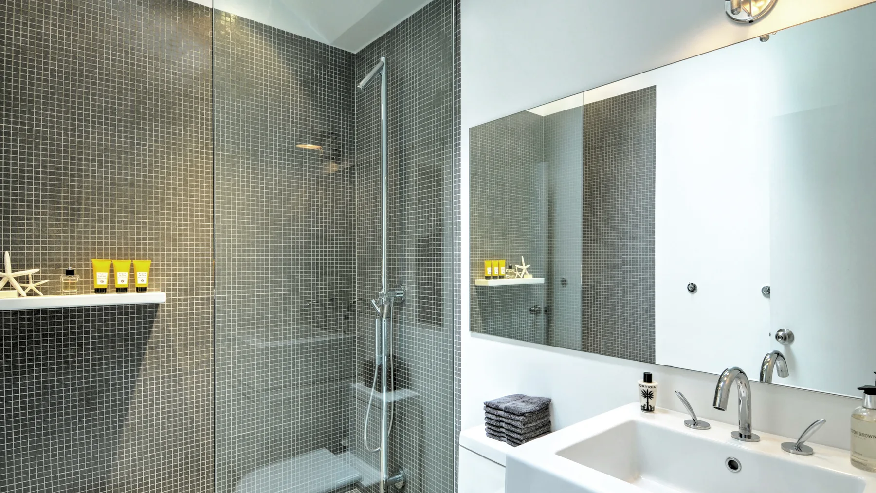 A tiled bathroom with a glass shower, sink, and large wall mirror.
