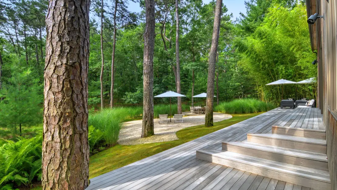 A wooden deck overlooks a landscaped outdoor seating area among trees.