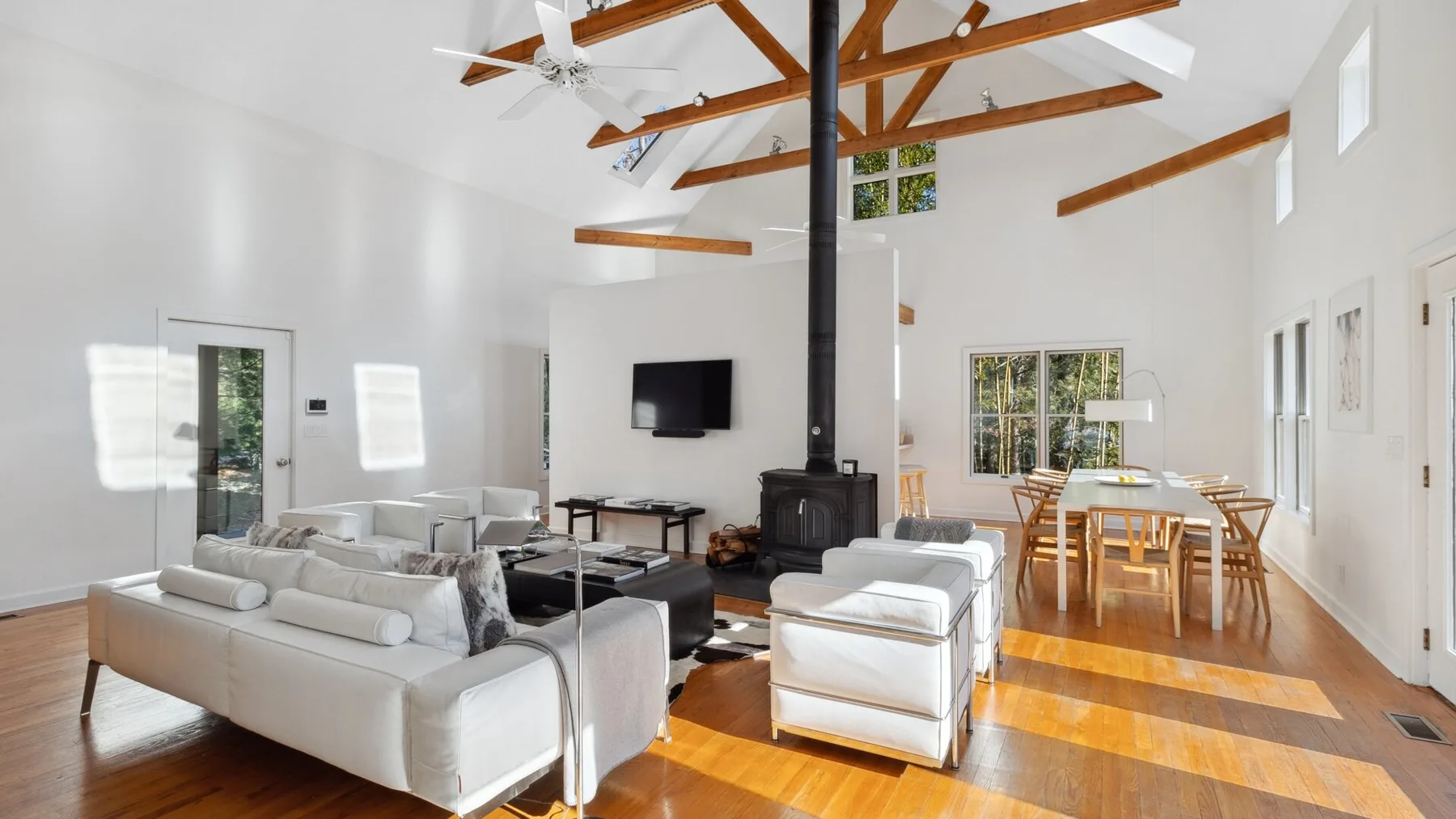 A bright open living and dining room with seating, a television, and a wooden dining table.