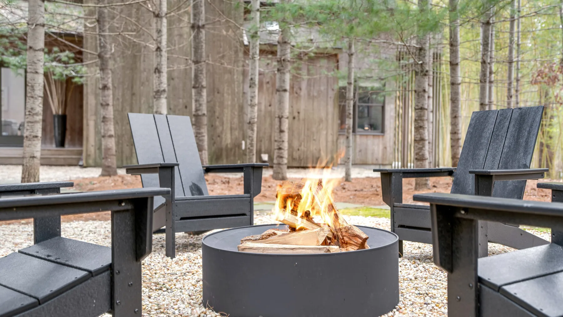 An outdoor fire pit sits among dark seating in a wooded courtyard.