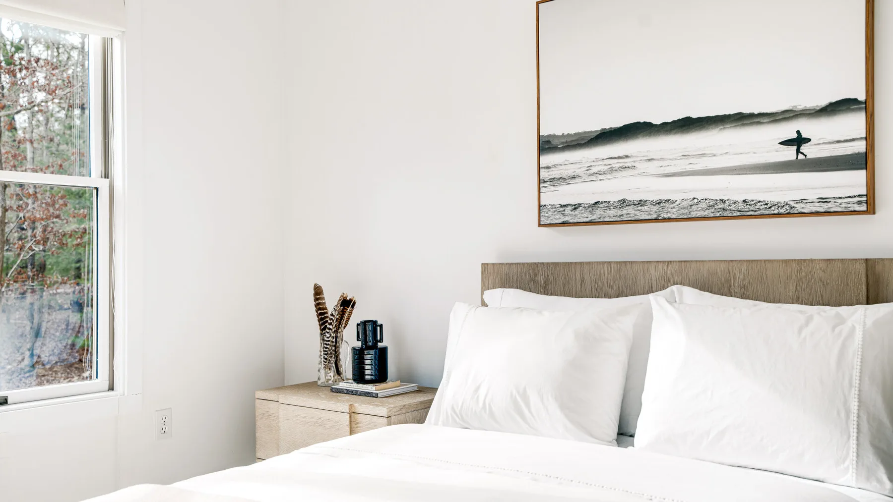 A bright bedroom with white bedding and a framed ocean photograph above the bed.
