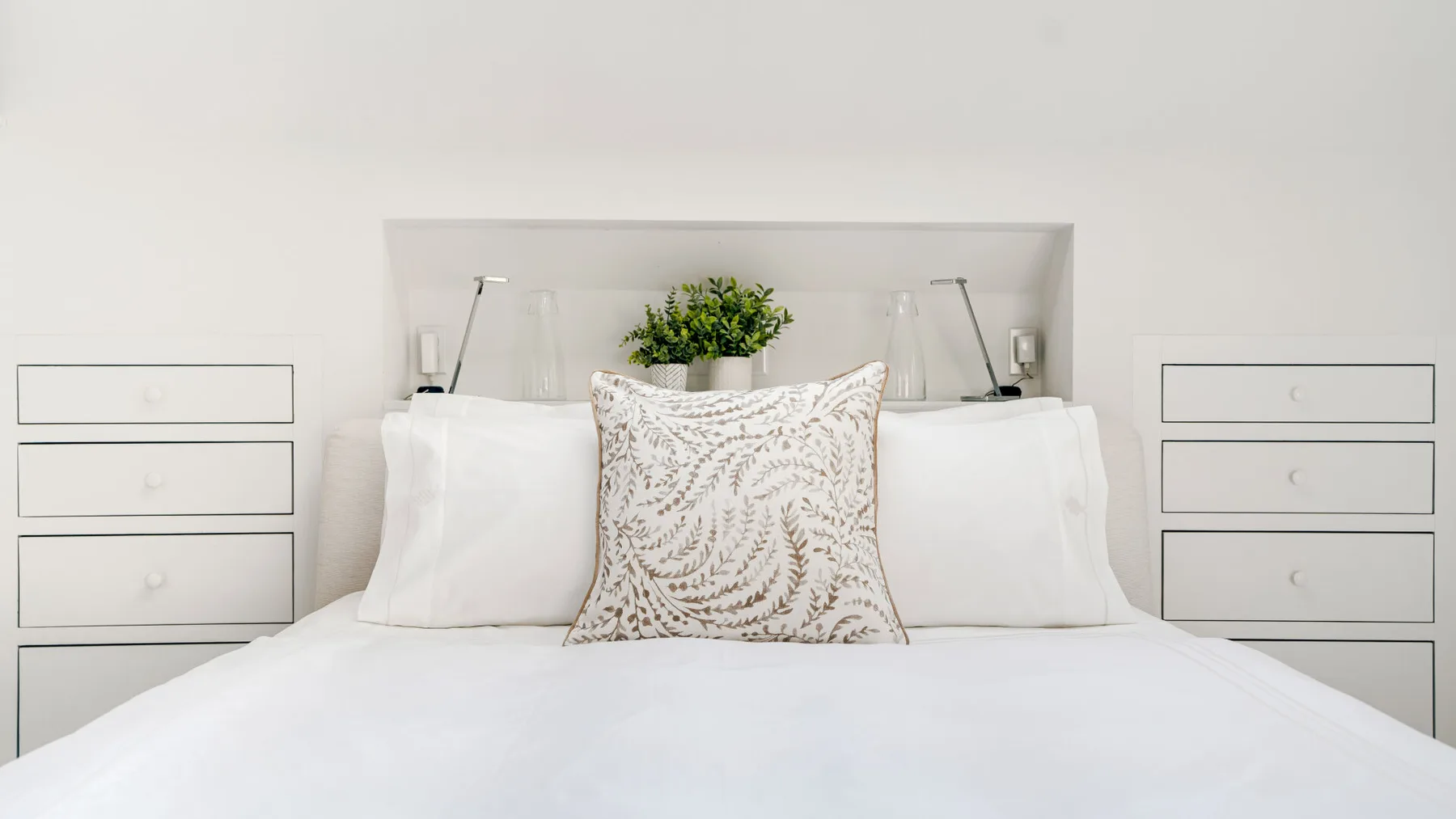 A neatly made bed with white bedding and a decorative pillow.