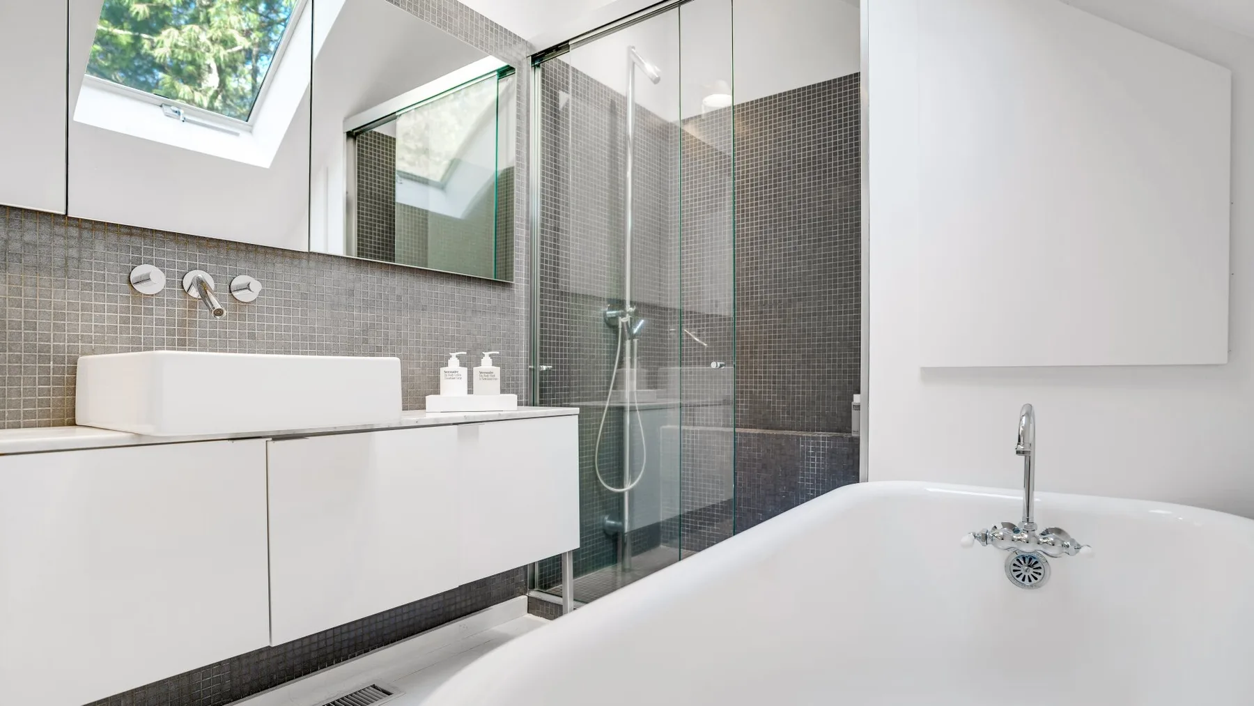 A bright bathroom with a glass shower, wall-mounted vanity, and freestanding tub.