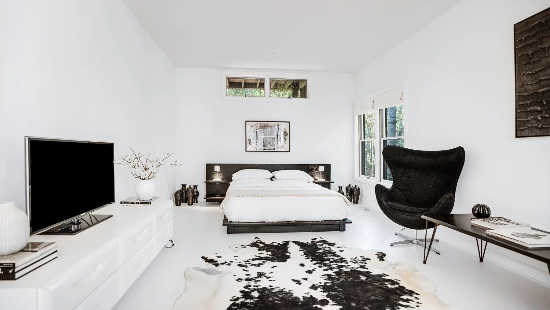 A bright bedroom with a bed, a television, and a dark lounge chair.
