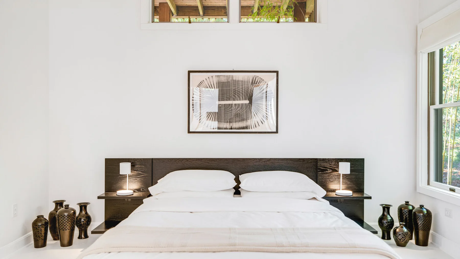 A bright bedroom with a neatly made bed and framed artwork above the headboard.