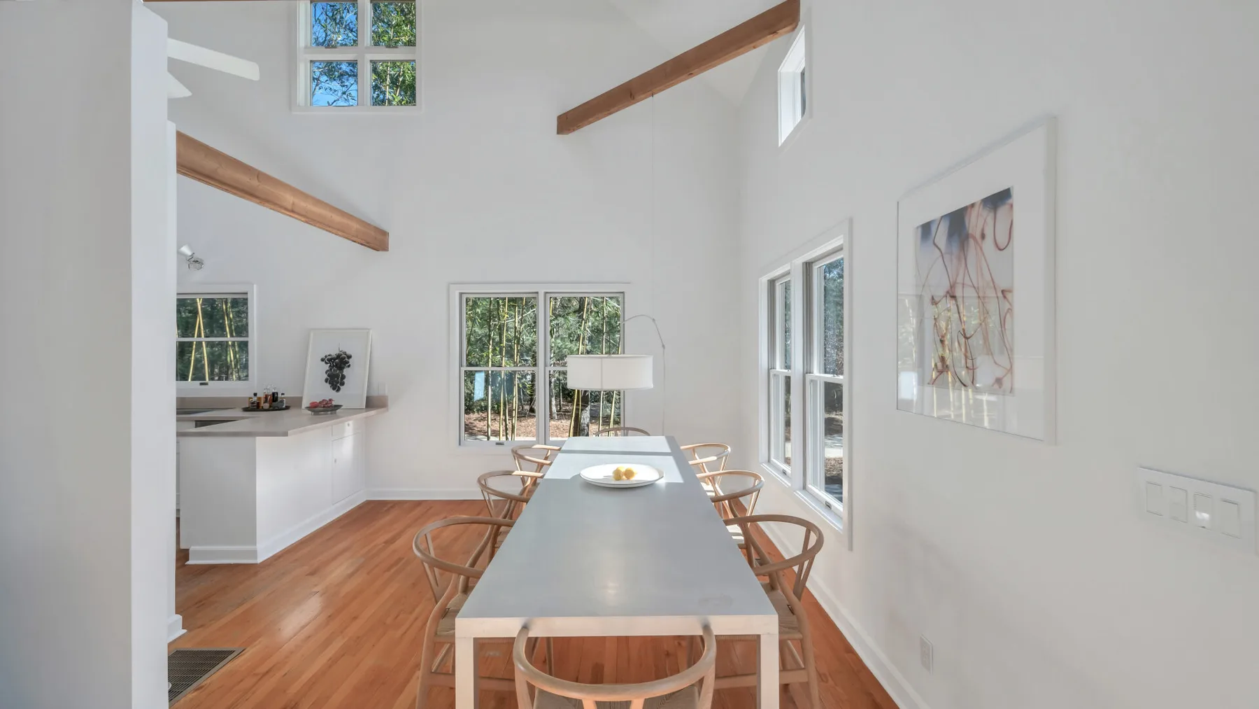 A bright dining area with a long table and windows overlooking trees.