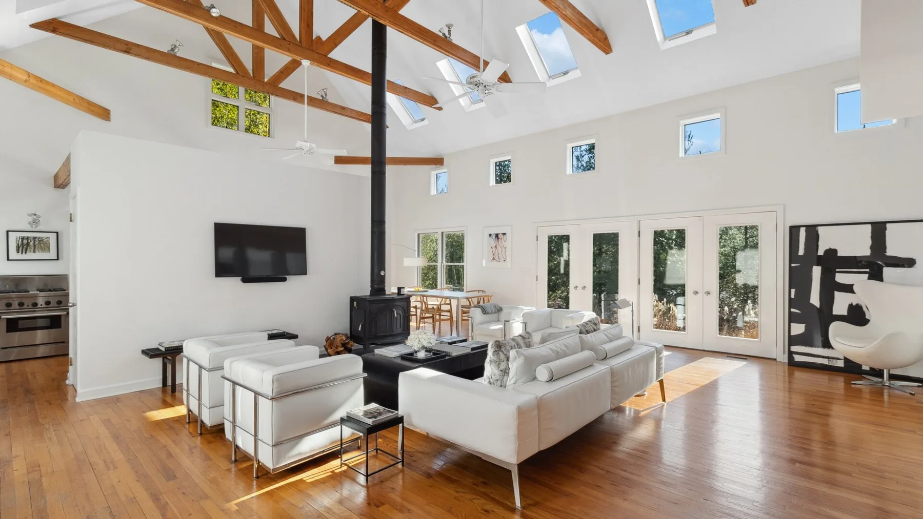 A bright living room with sofas, a wood-burning stove, and exposed ceiling beams.