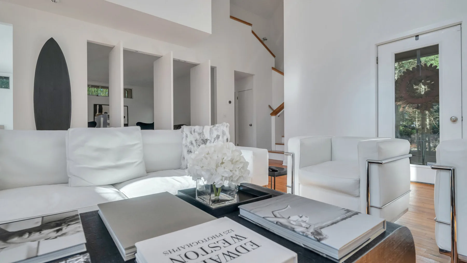 A bright living room with white seating and a glass door opening to a patio.