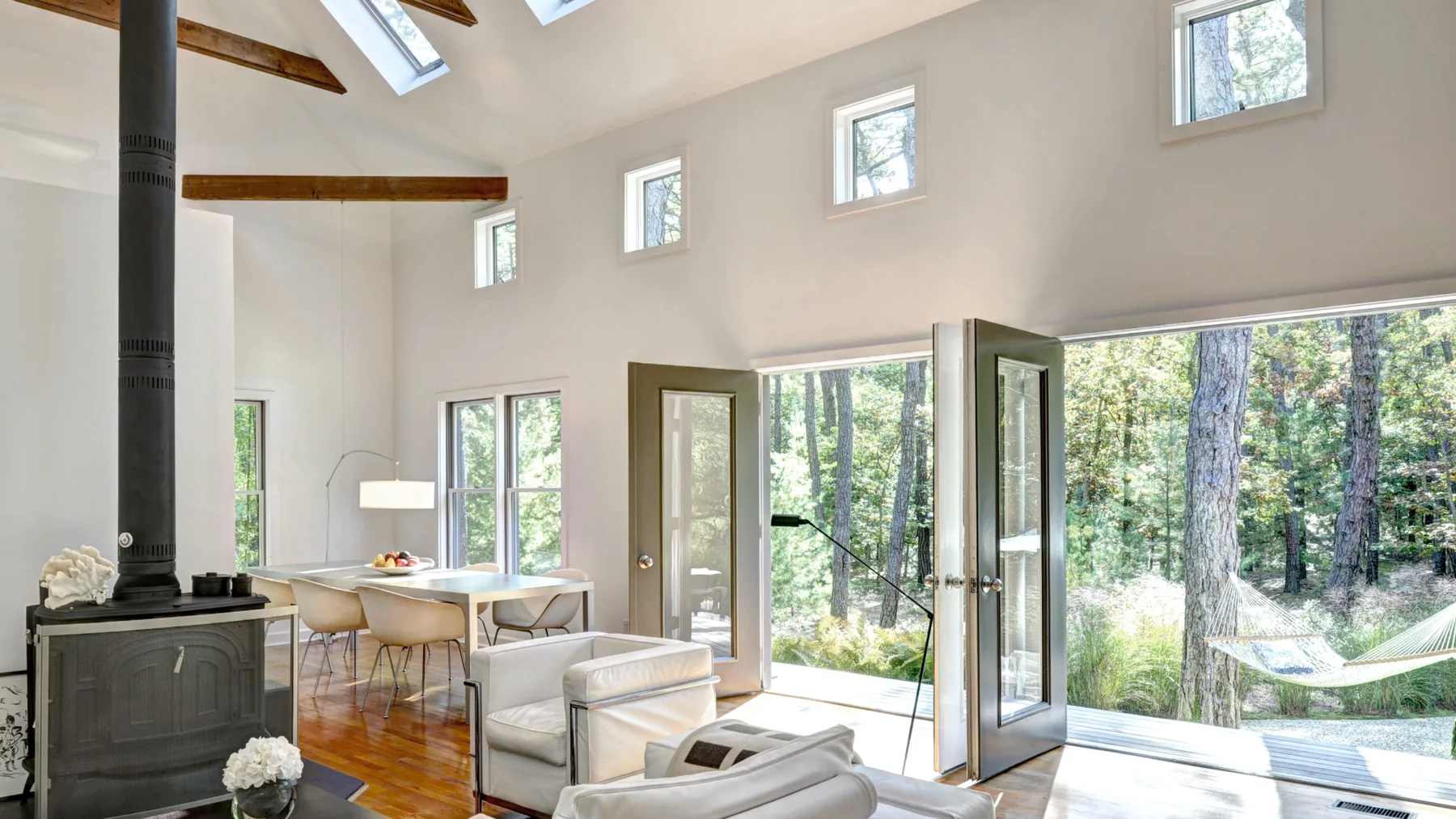 A bright living area opens onto a wooded patio, with seating and a dining table.