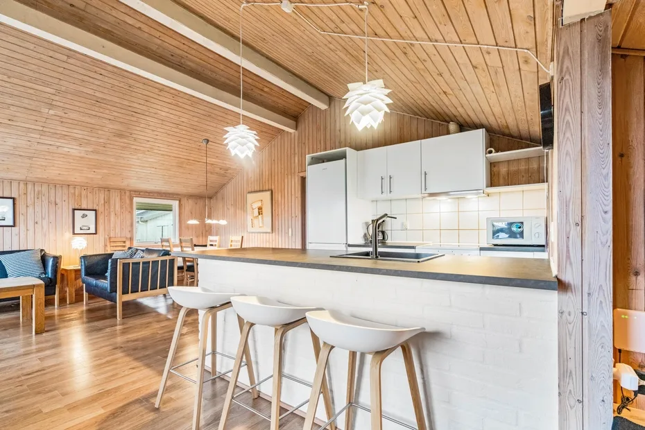 Una cocina luminosa con barra y taburetes se abre a una sala revestida de madera.