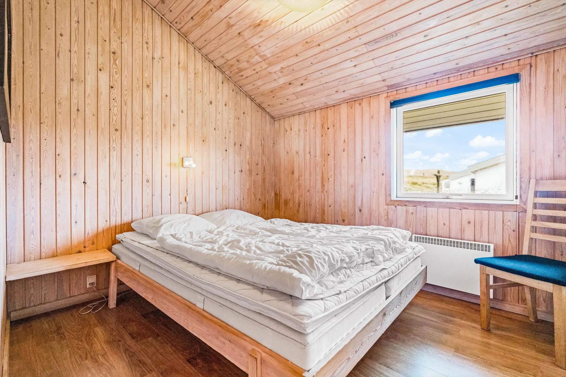 Un dormitorio con una cama junto a una ventana y una silla de madera.