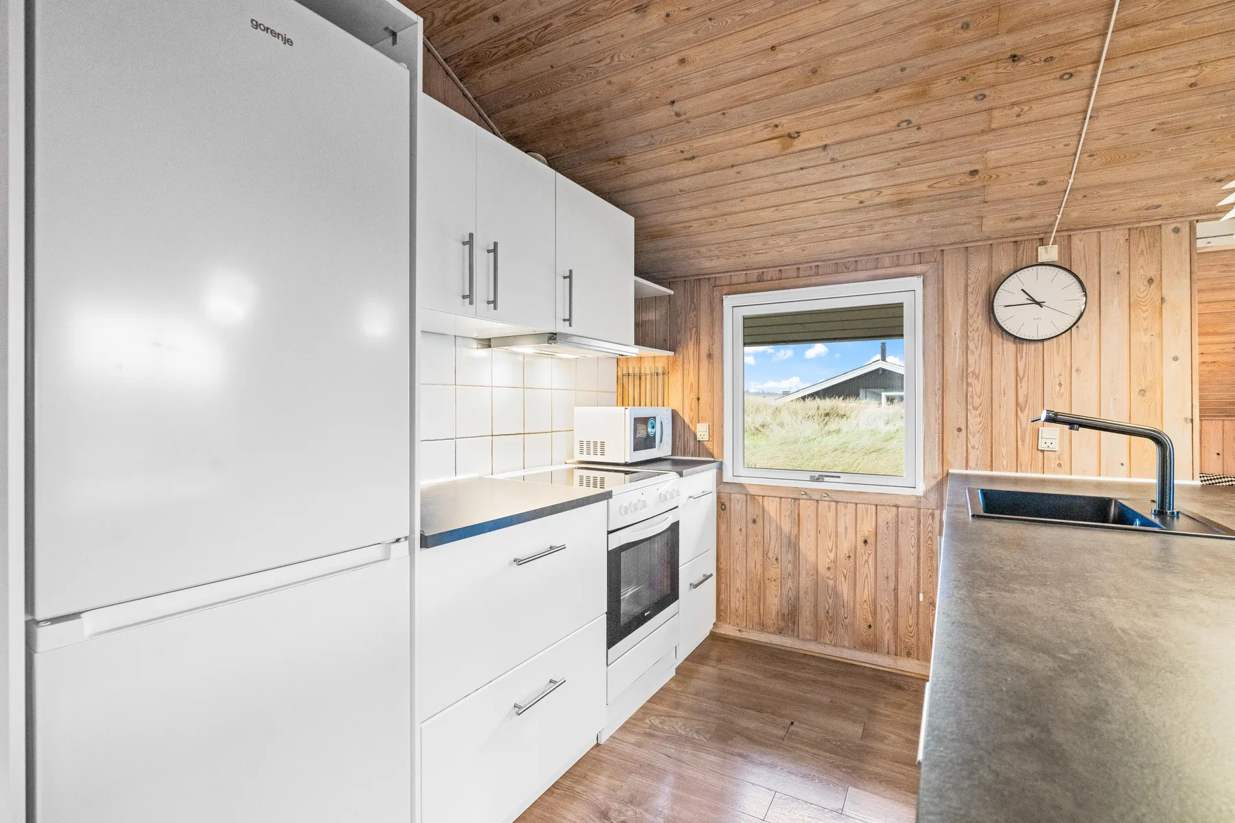 Una cocina luminosa con gabinetes blancos, refrigerador y ventana.