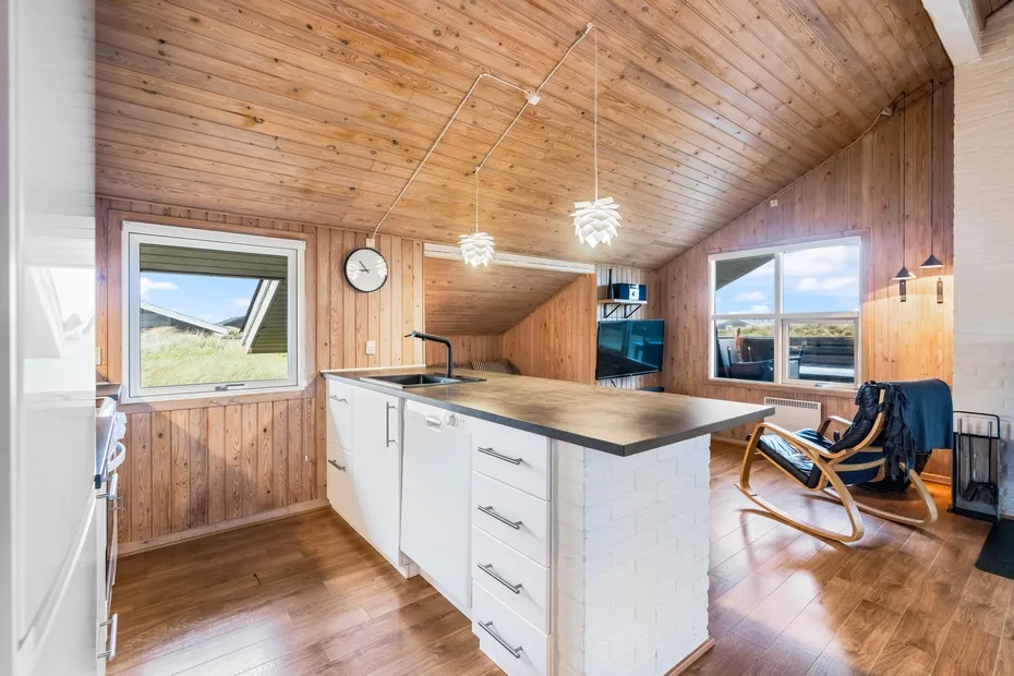 Una cocina revestida de madera con una isla blanca y ventanas que dan al exterior.