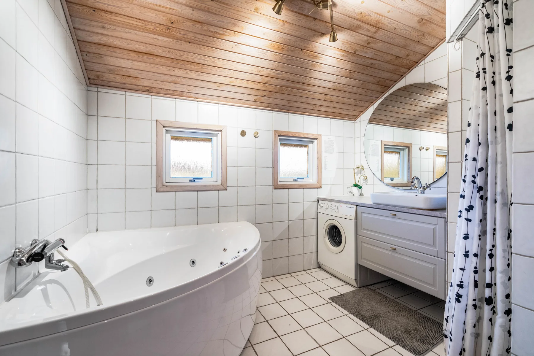 Baño con azulejos, bañera, lavabo con mueble, lavadora y cortina de ducha.