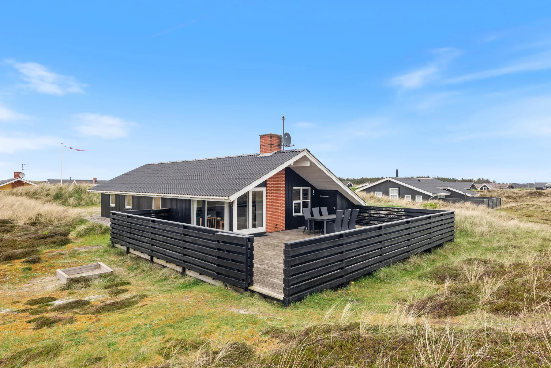 Una casa moderna está entre dunas cubiertas de hierba, con una terraza cercada.
