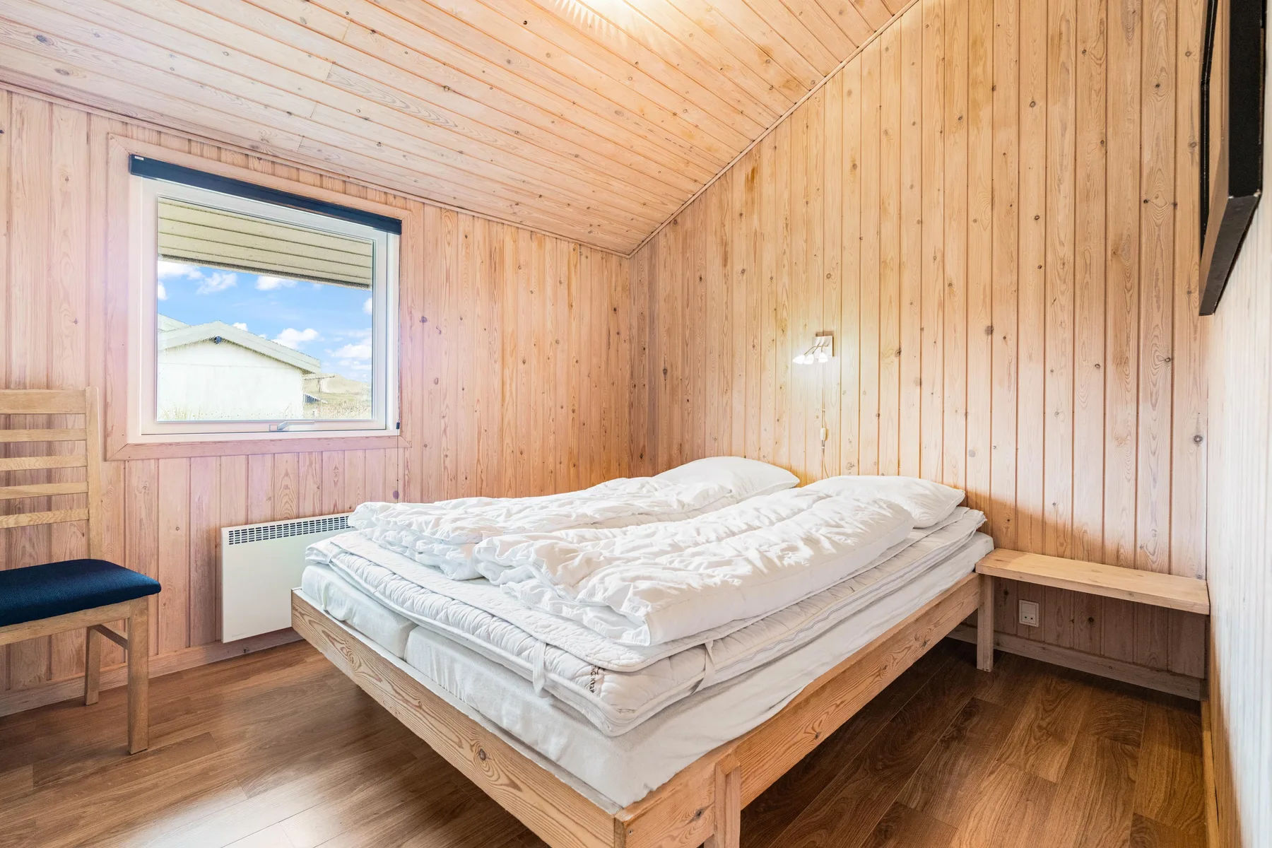 Un dormitorio revestido de madera con cama, ventana y banco.