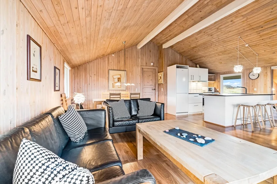 Una sala con paneles de madera, asientos oscuros y una cocina abierta.