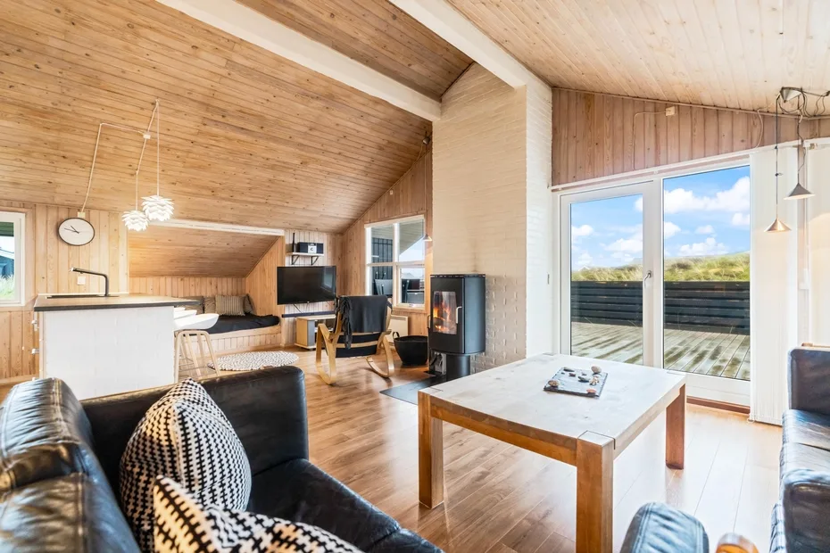 Sala de estar revestida de madera con asientos, una mesa de comedor y puertas de vidrio.