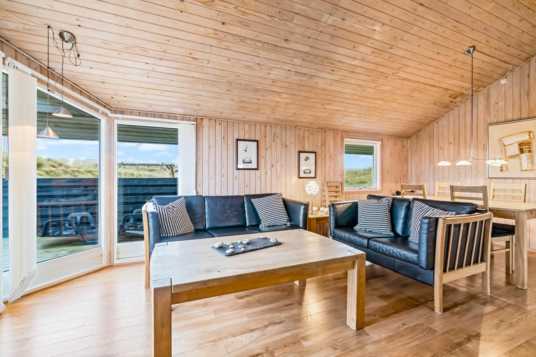 Sala de estar con paneles de madera, asientos alrededor de una mesa de centro y grandes ventanas.