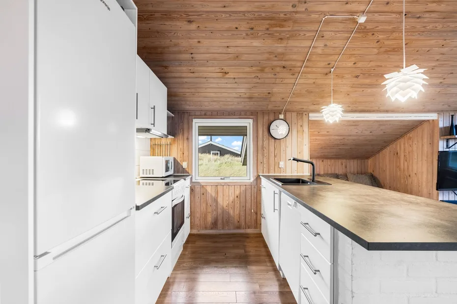 Una cocina compacta con gabinetes blancos, una isla central y paredes revestidas de madera.