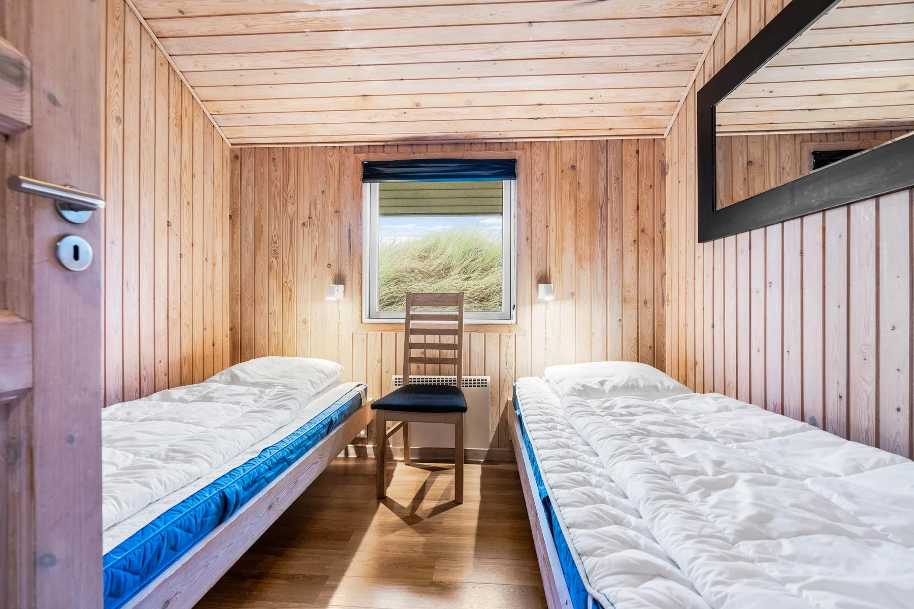 Dormitorio con paneles de madera, dos camas individuales y una silla bajo la ventana.