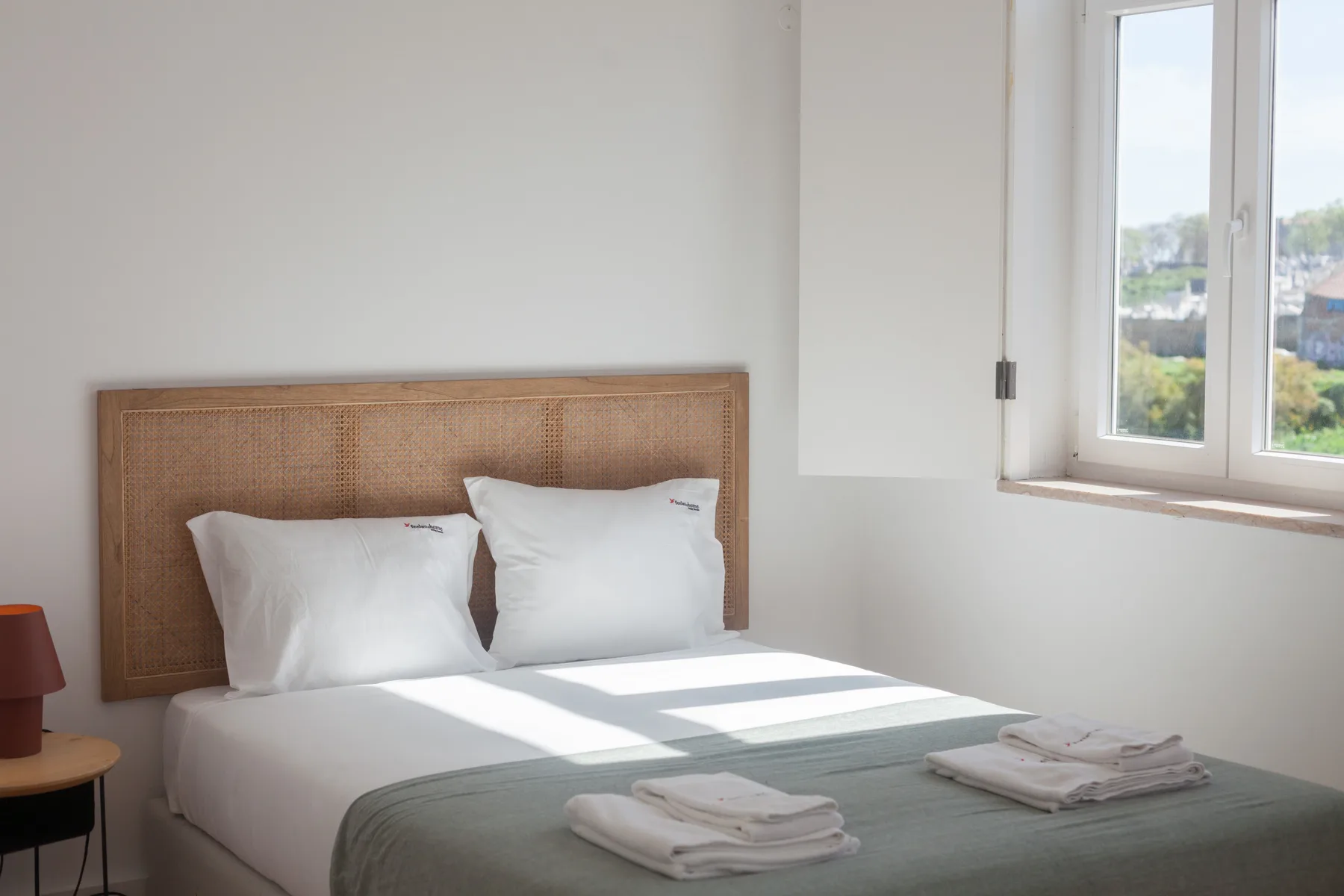 A bright bedroom with a bed, folded towels, and a window.
