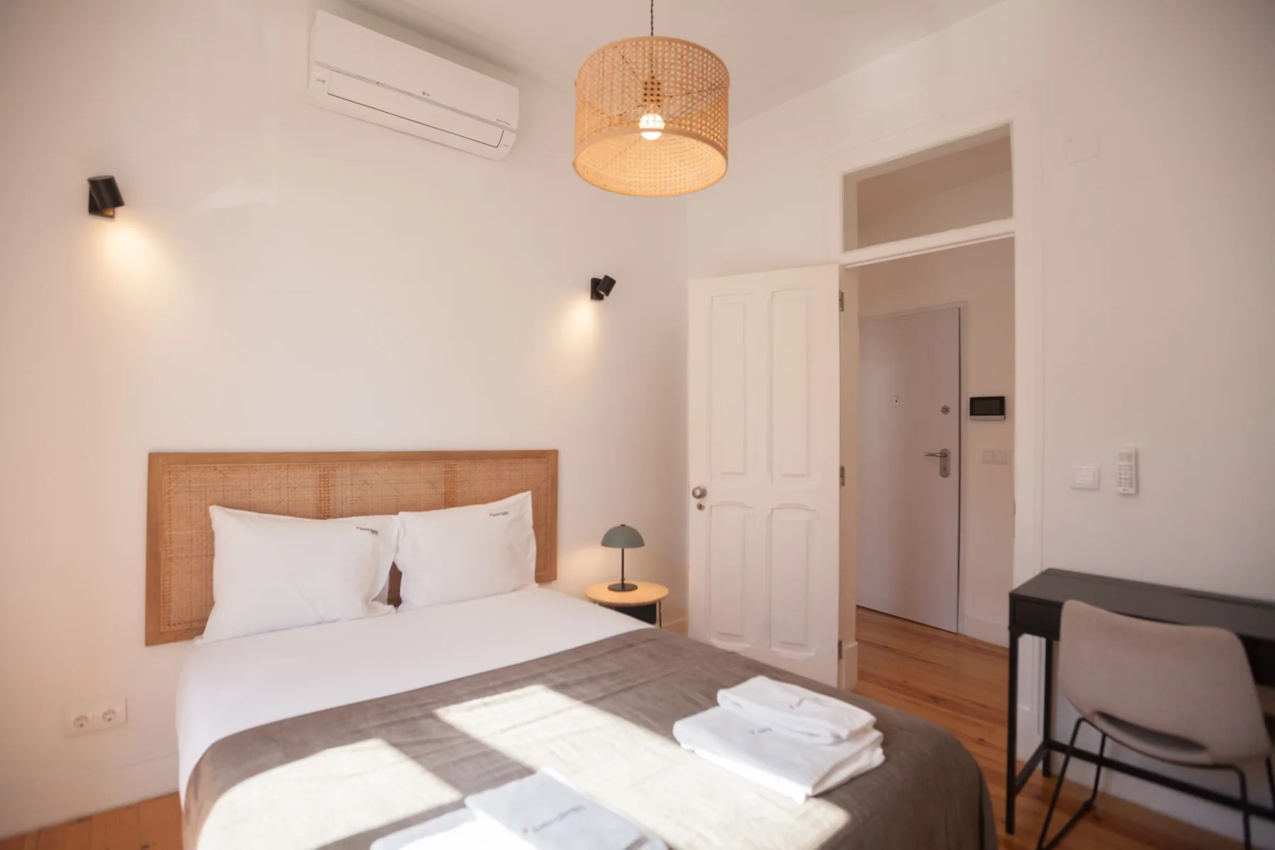 Bedroom with a bed, bedside table, and desk beside the open doorway.
