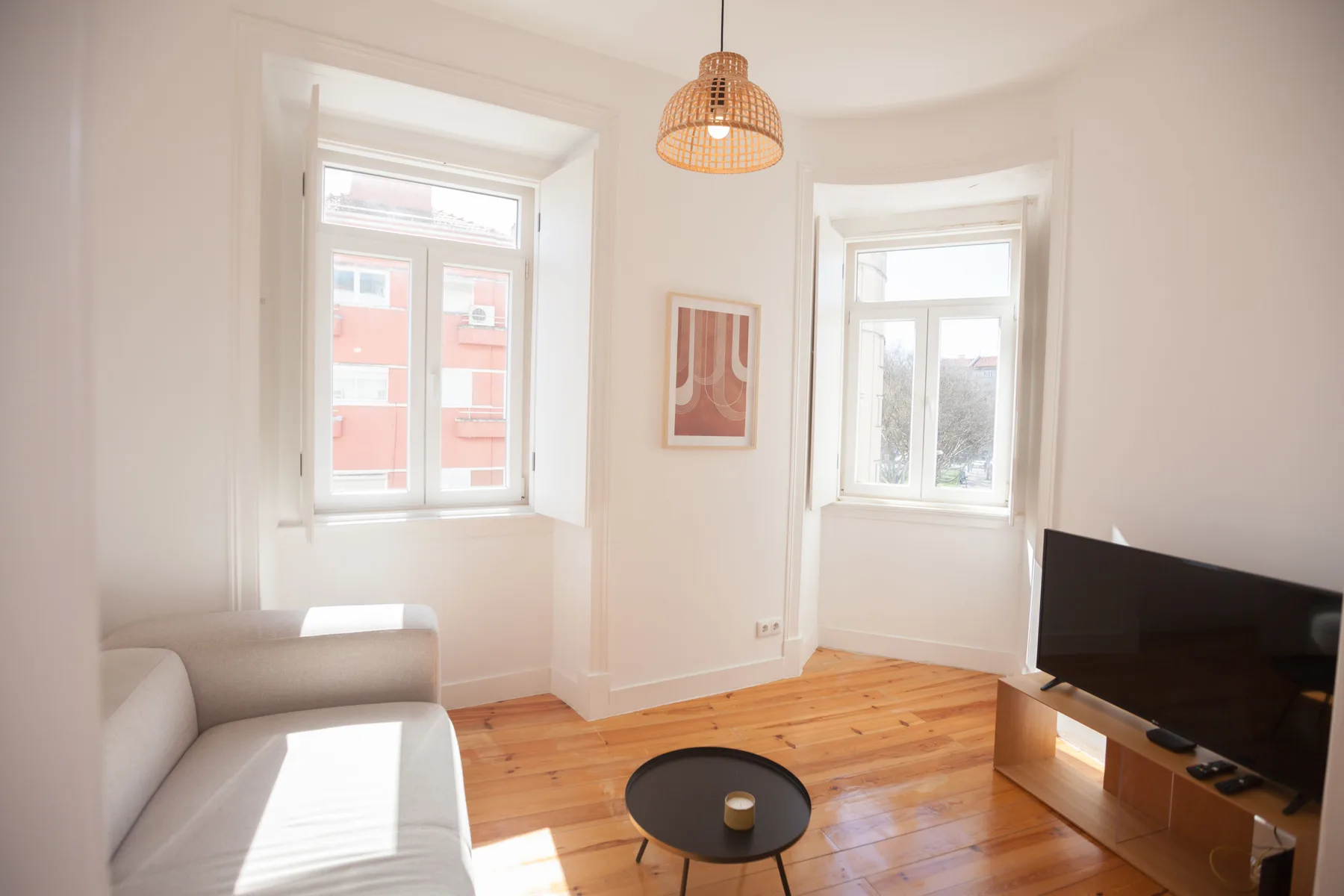 Bright living room with a light sofa, wooden floor, and television.
