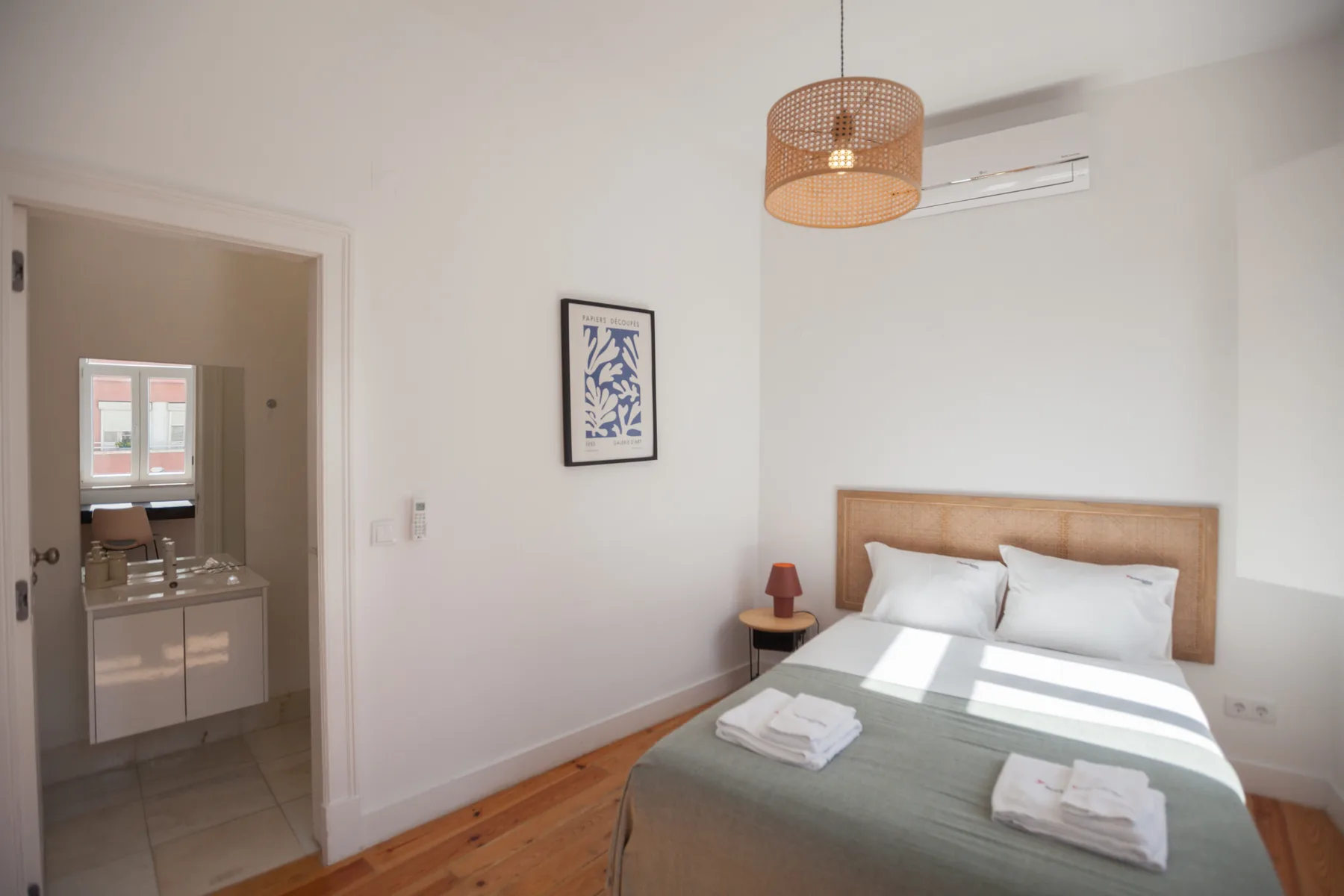 A bedroom with a bed, folded towels, and a framed print on the wall.