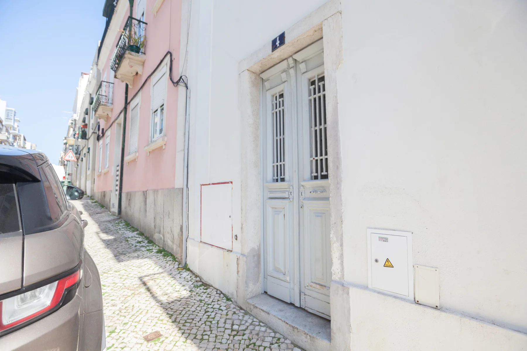 A cobblestone street runs beside pastel building façades and a parked car.