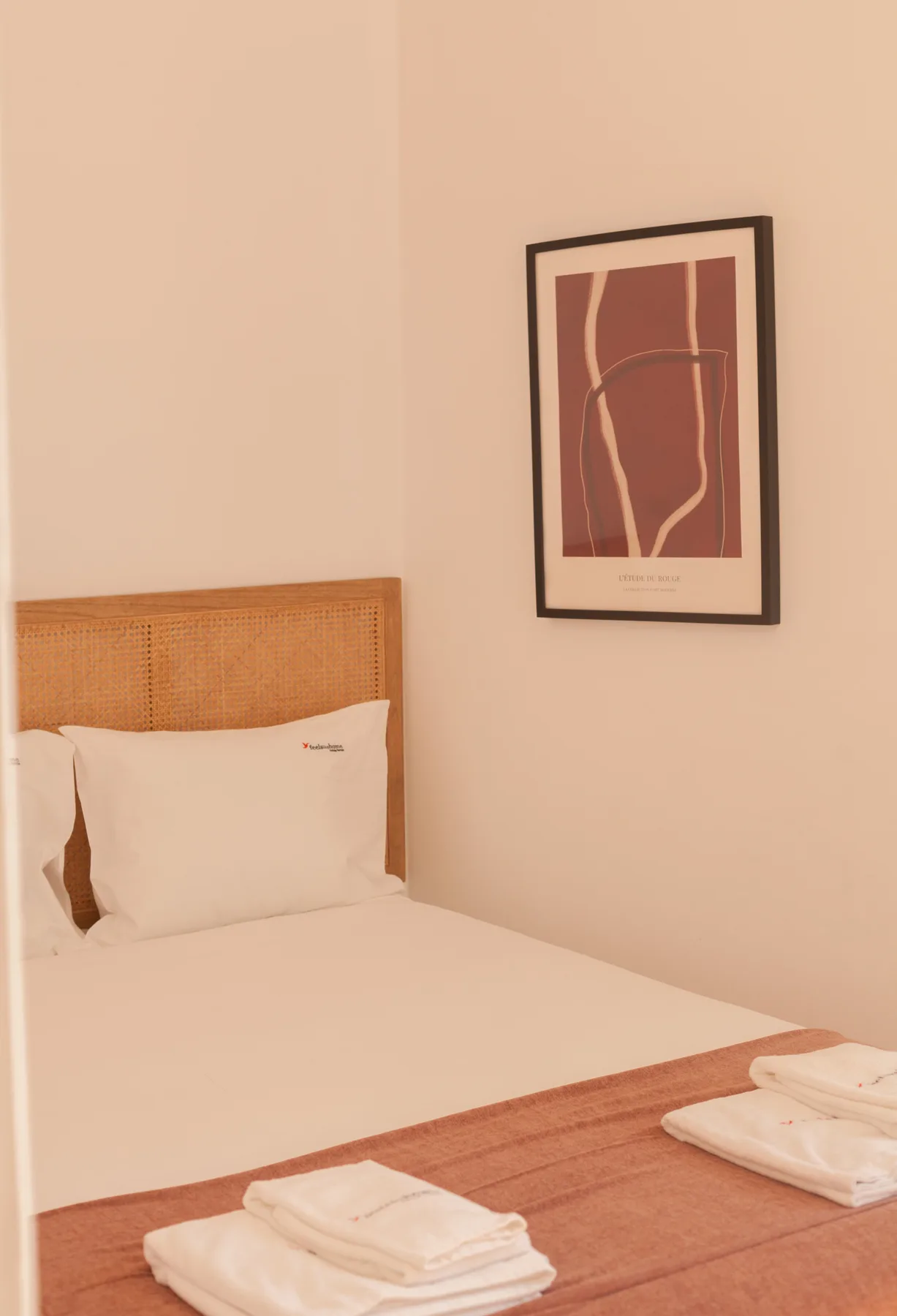 Un dormitorio ordenado con una lámina abstracta enmarcada sobre la cama.