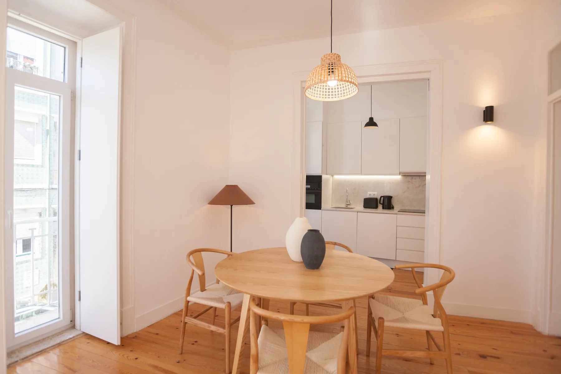A dining area with a round wooden table and an open kitchen beyond.