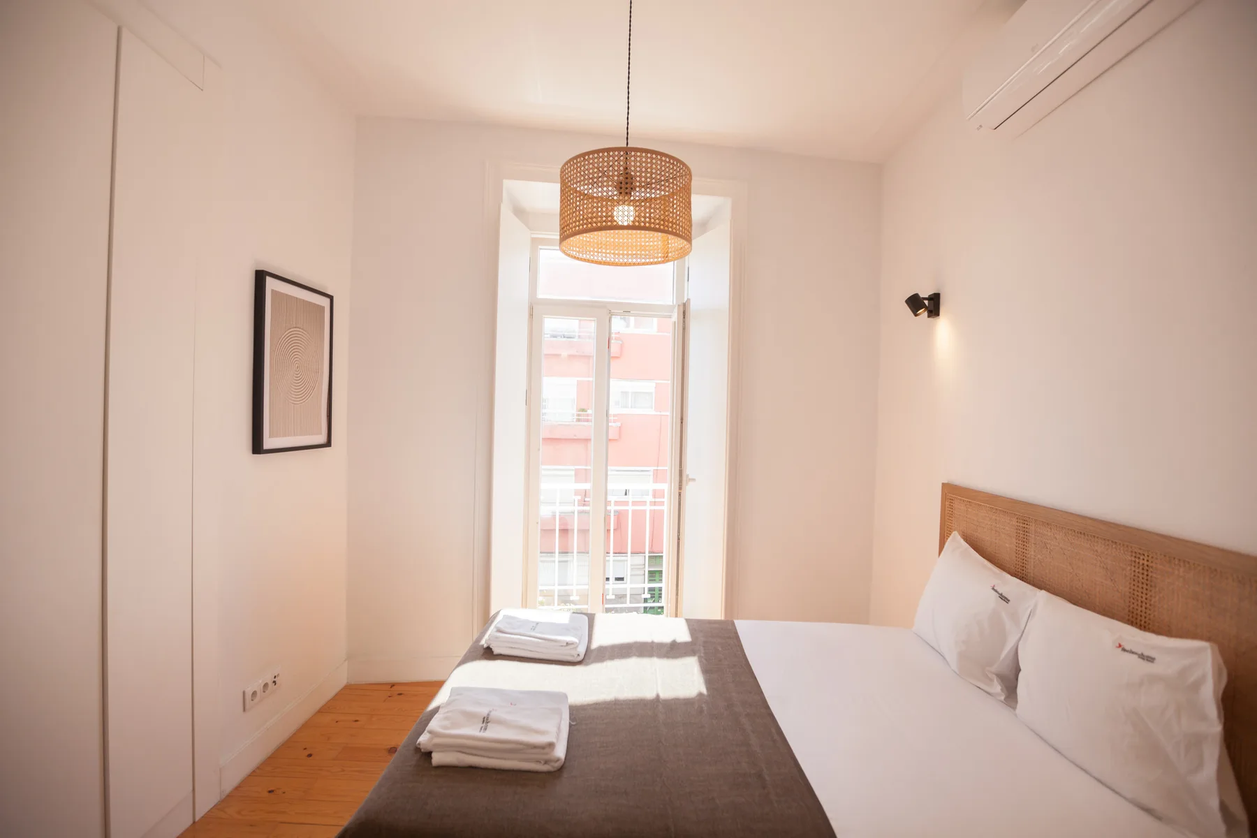 A bright bedroom with a bed, folded towels, and a window.