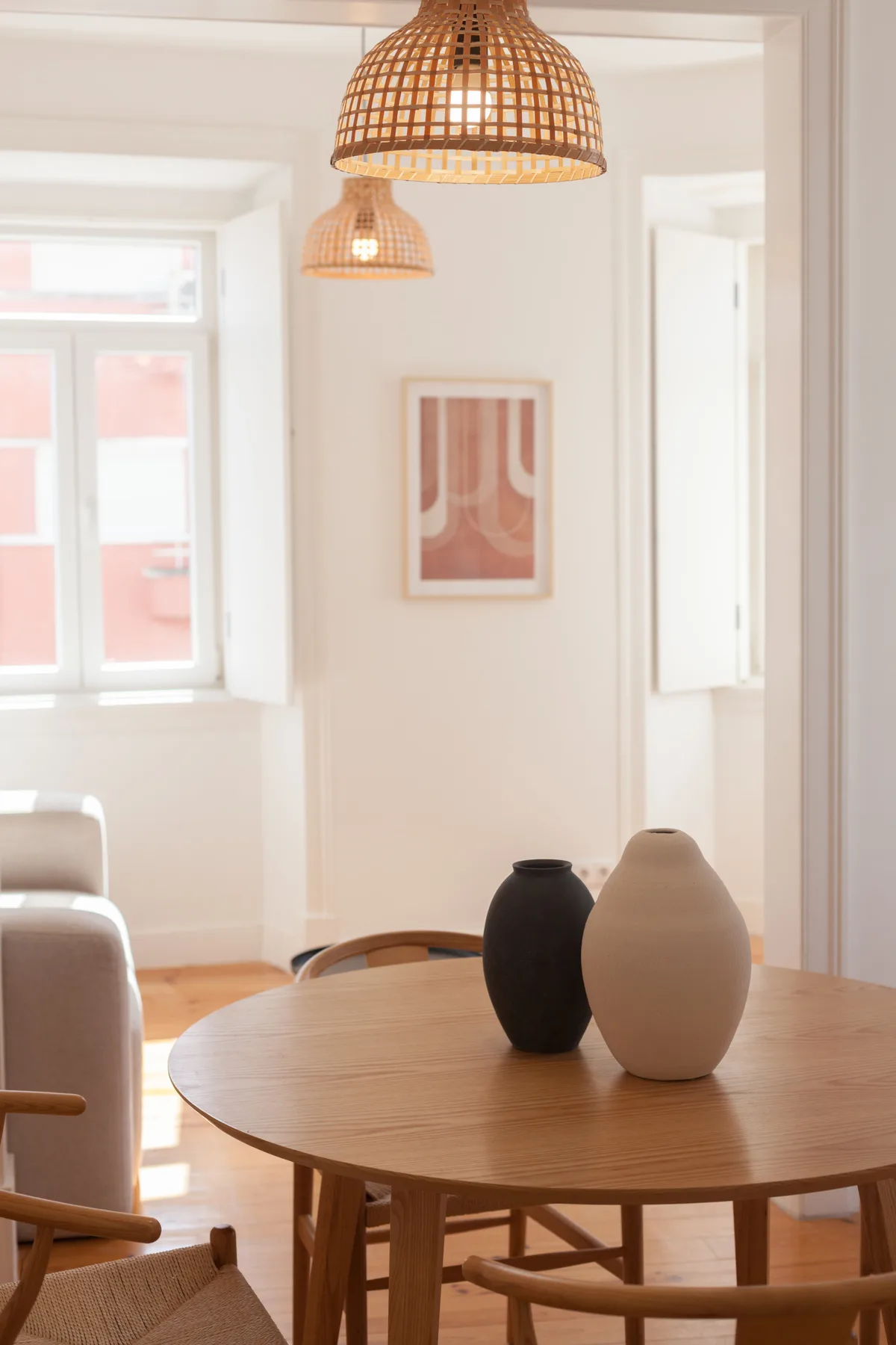 A bright dining area with a round wooden table and woven pendant lights.