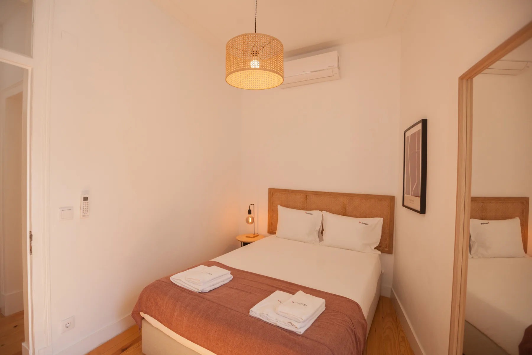 Un dormitorio con una cama, toallas dobladas y un aire acondicionado en la pared.