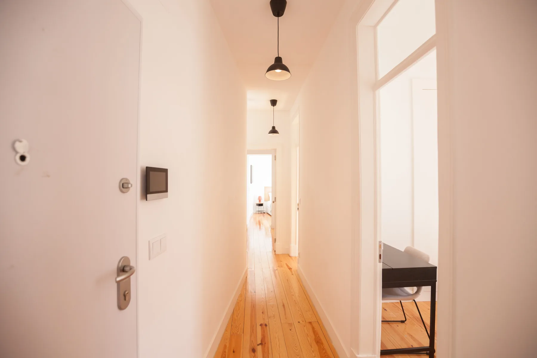 A bright apartment hallway has wooden flooring and several open doorways.