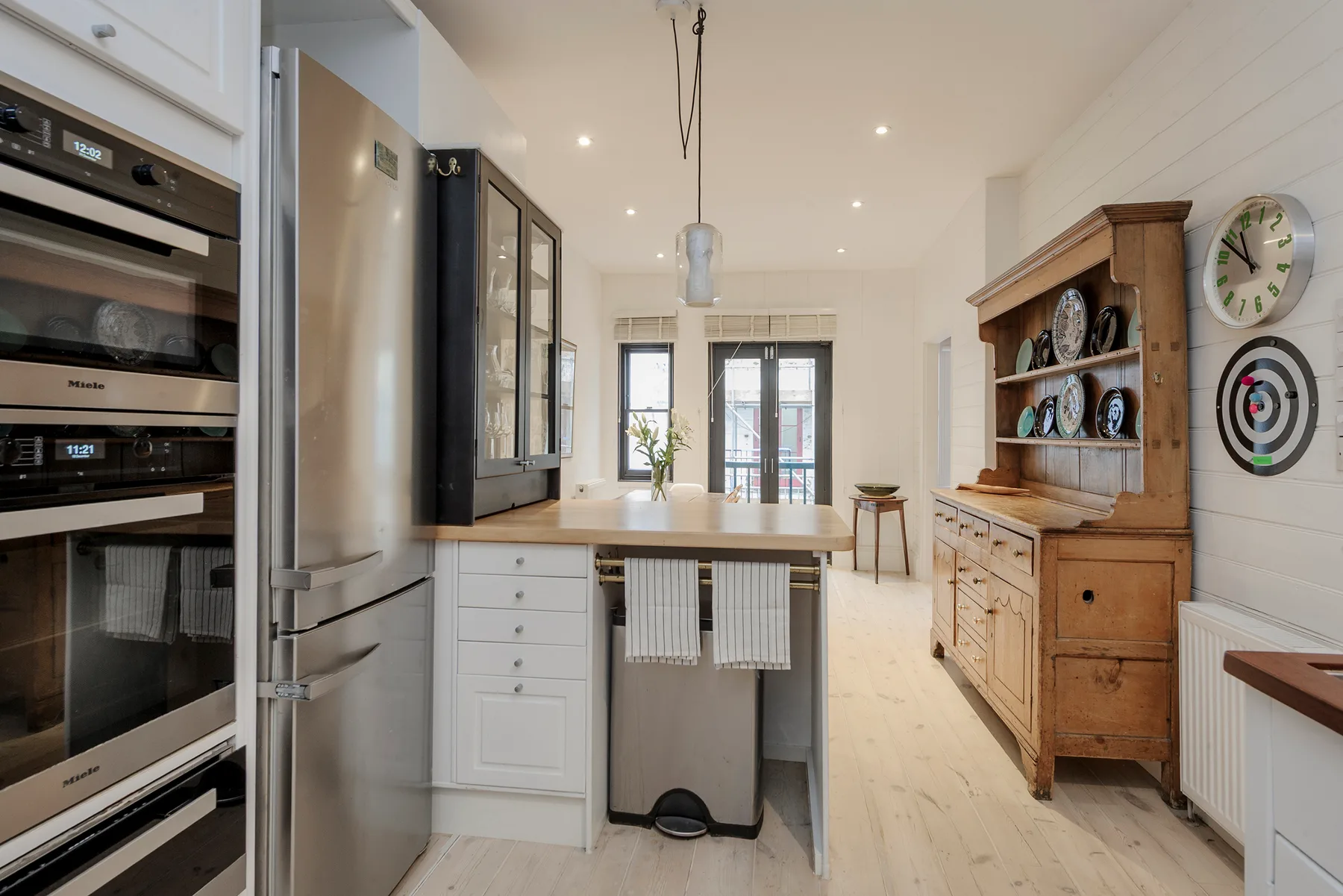 A bright kitchen with an island, stainless steel appliances, and a wooden hutch.