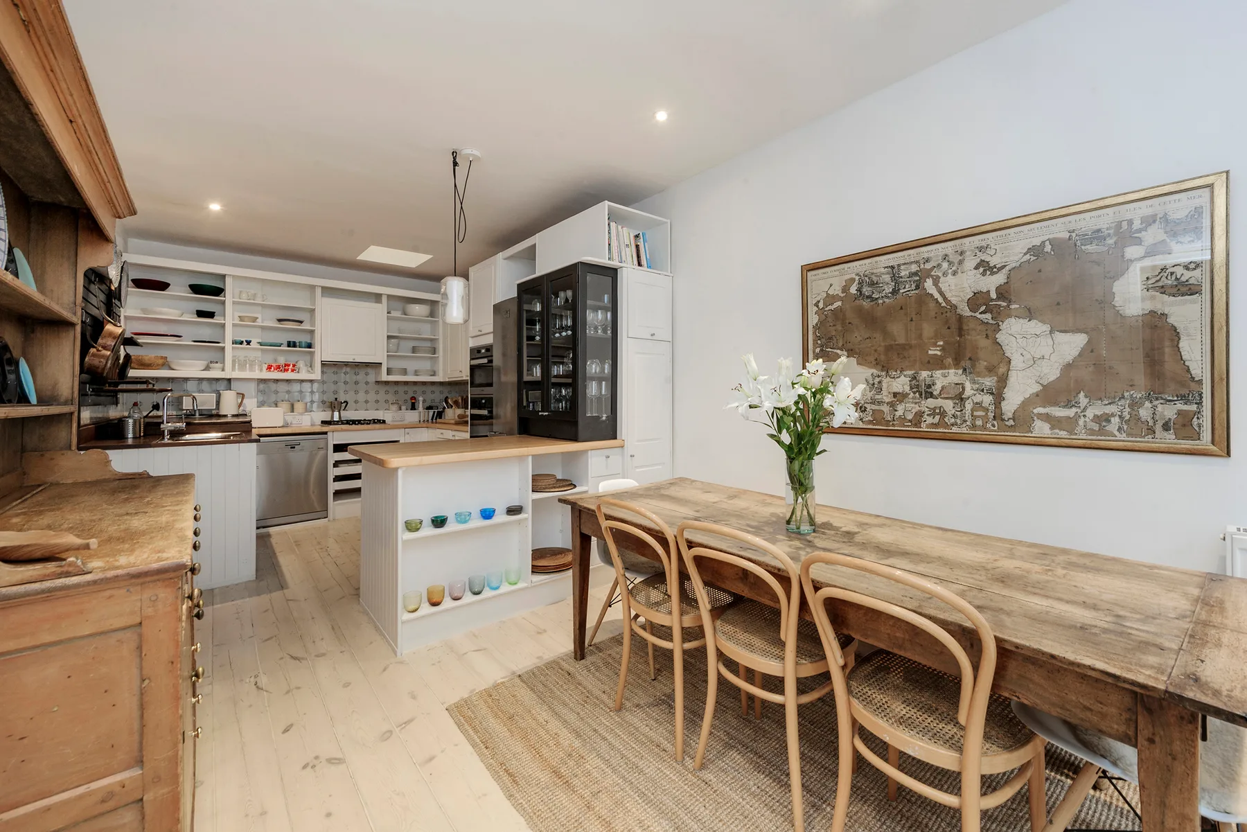 A bright kitchen and dining area with a long wooden table and open shelving.