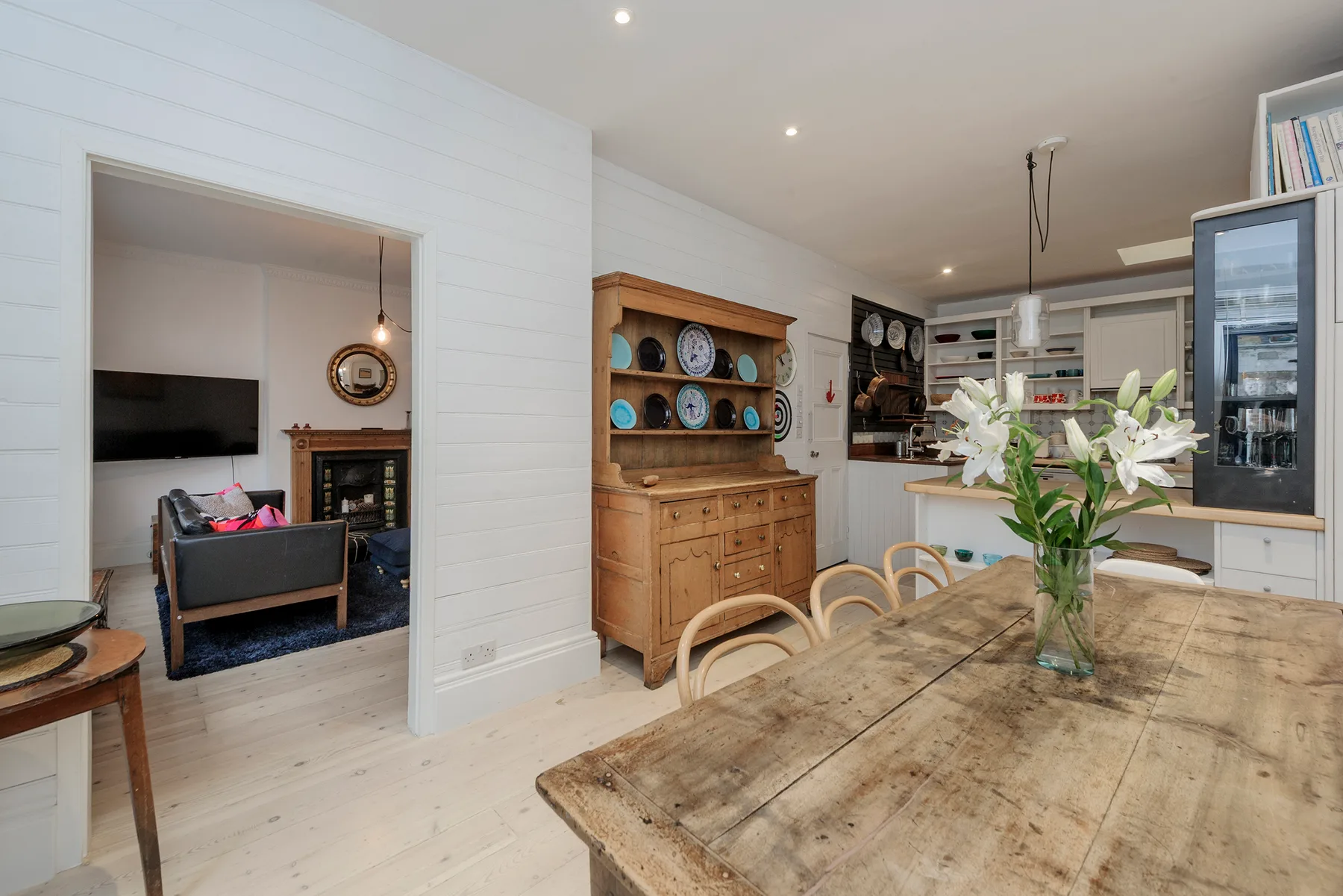 A dining area with a long wooden table and an open kitchen behind it.