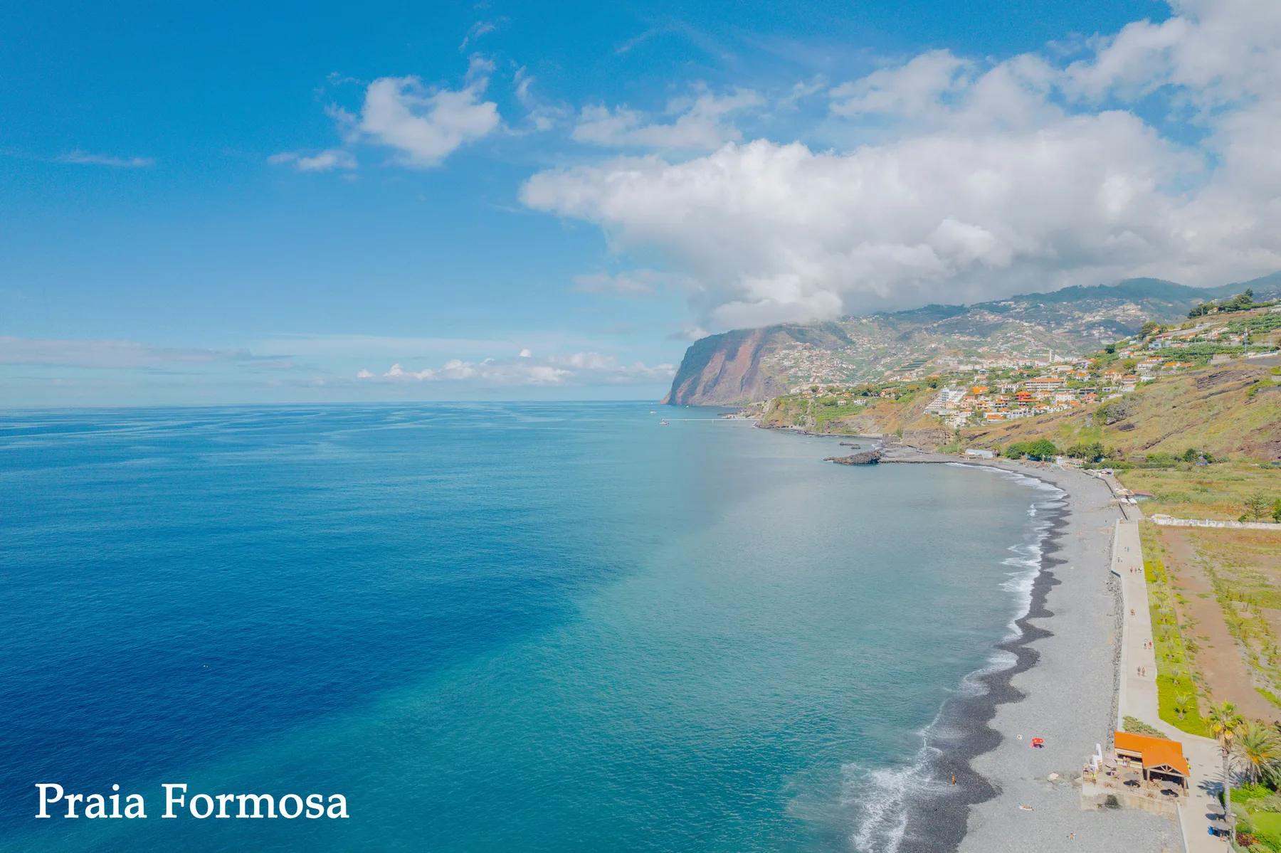 Aerial view of a coastline with a broad beach and hills in the distance.