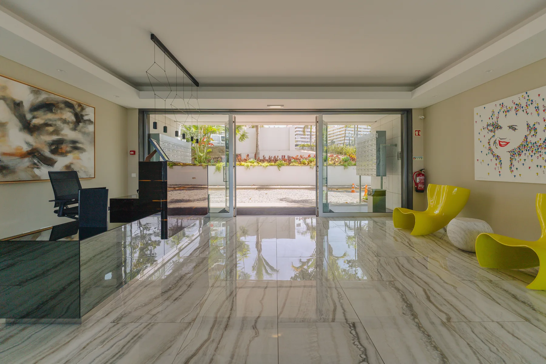 A bright lobby with a reception desk, seating, and glass doors opening to a landscaped courtyard.