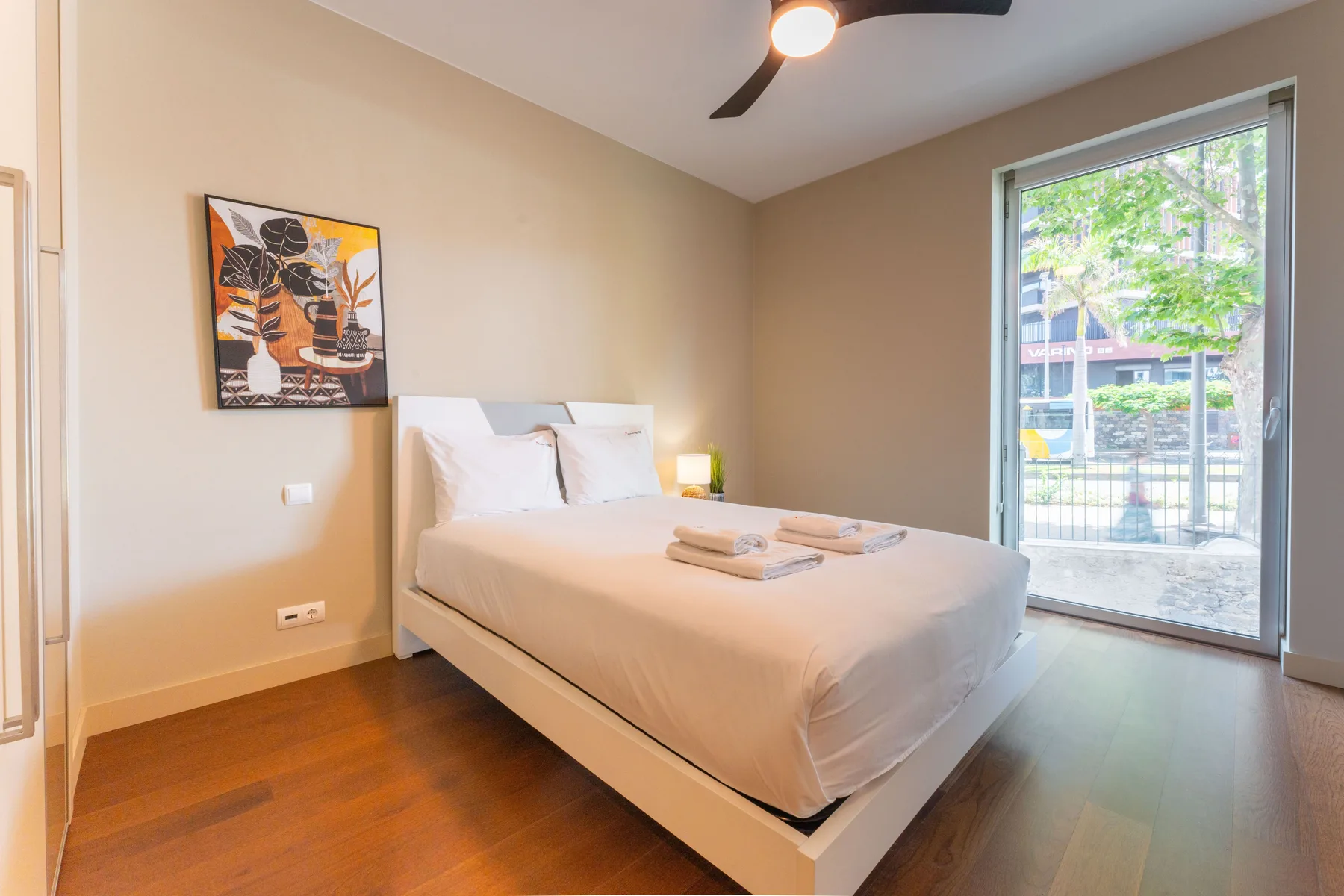 A bedroom with a bed, framed artwork, and a large window.