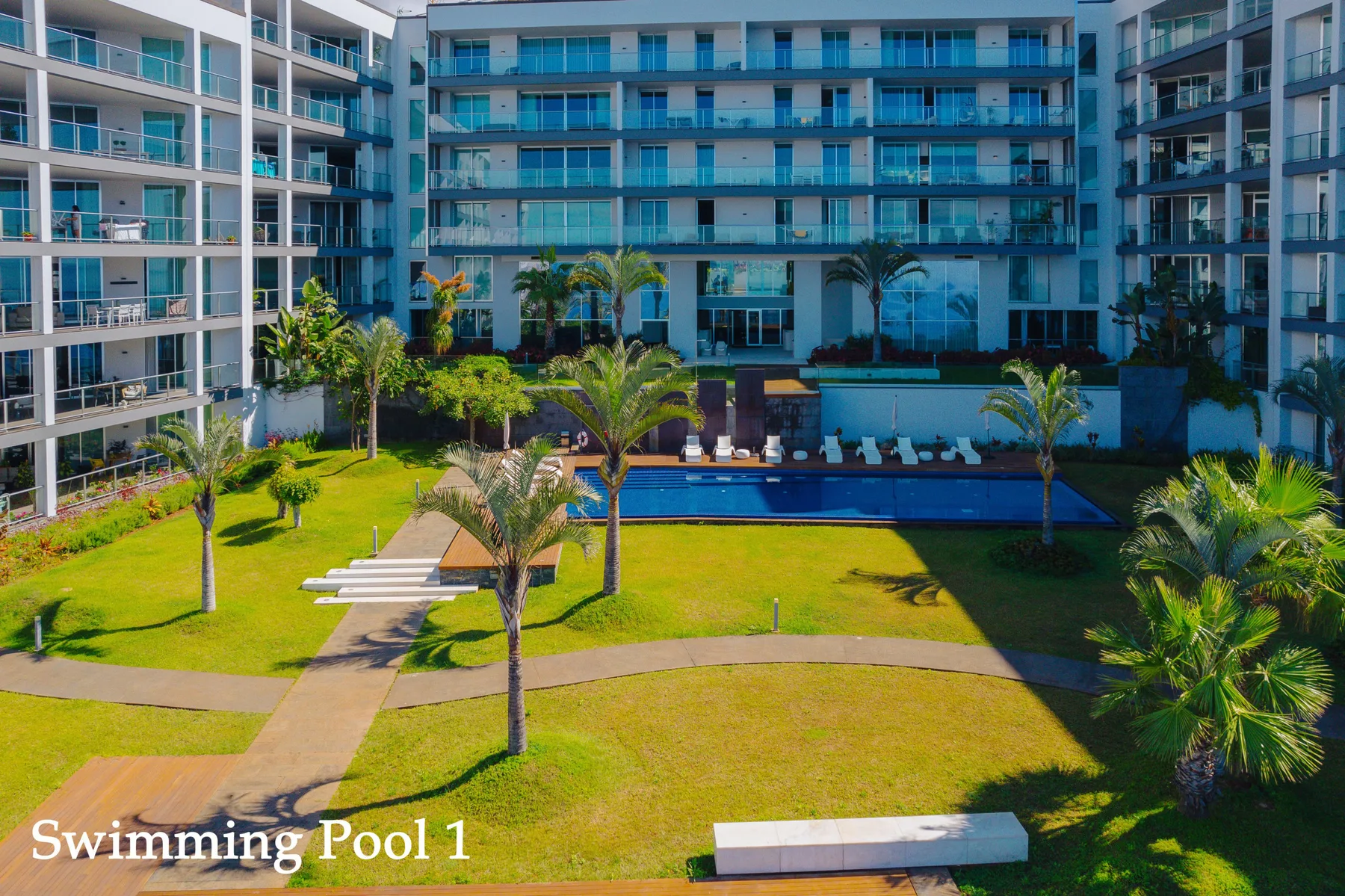 A landscaped courtyard with a swimming pool sits between modern apartment buildings.