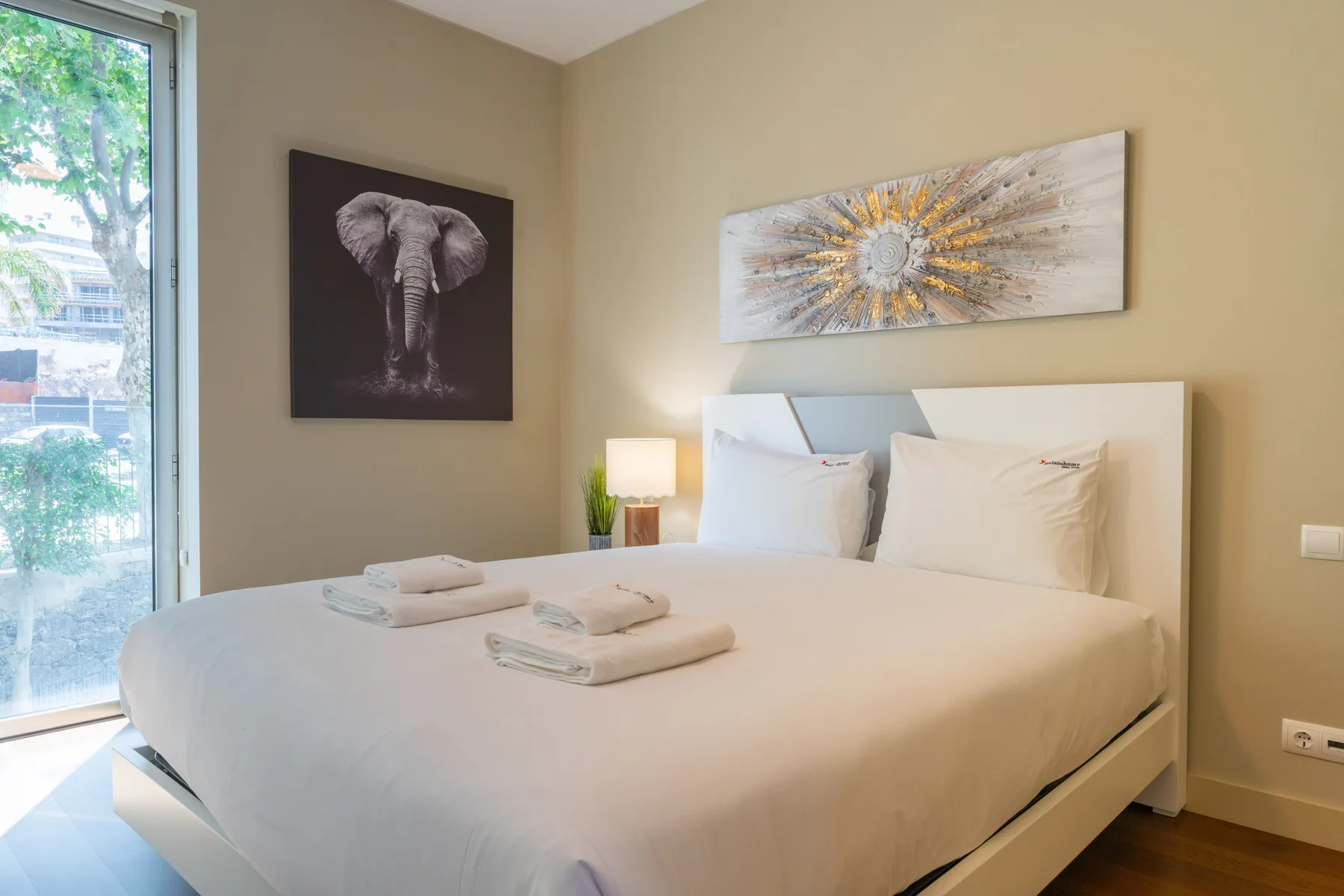 A bright bedroom with a neatly made bed and framed wall art.