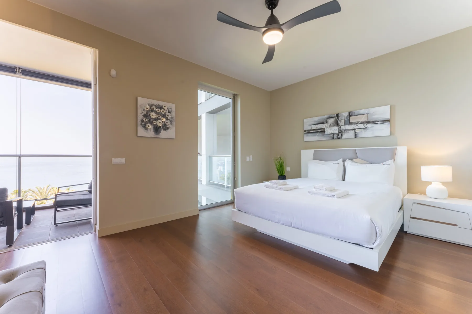 A bright bedroom with a neatly made bed and a glass door opening to a balcony.