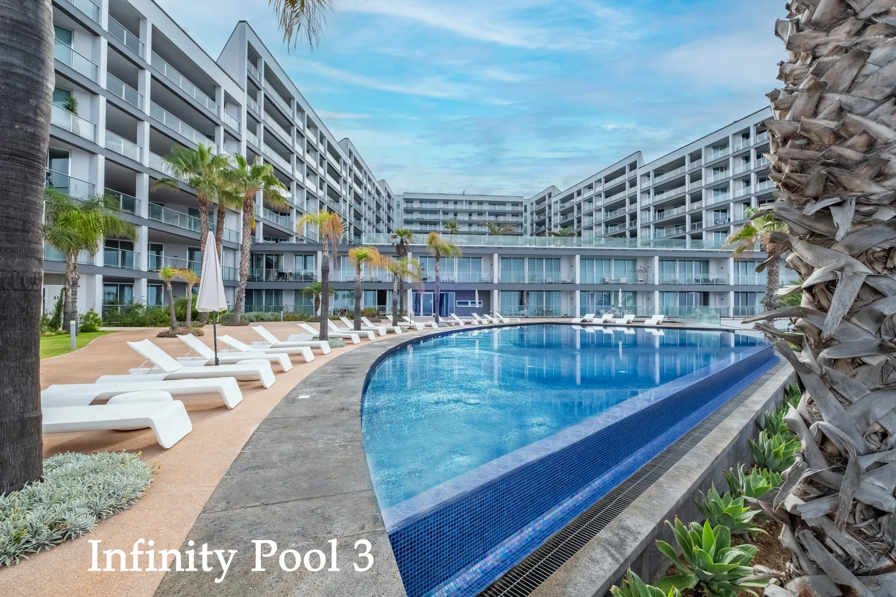 An outdoor swimming pool is surrounded by lounge seating and modern buildings.