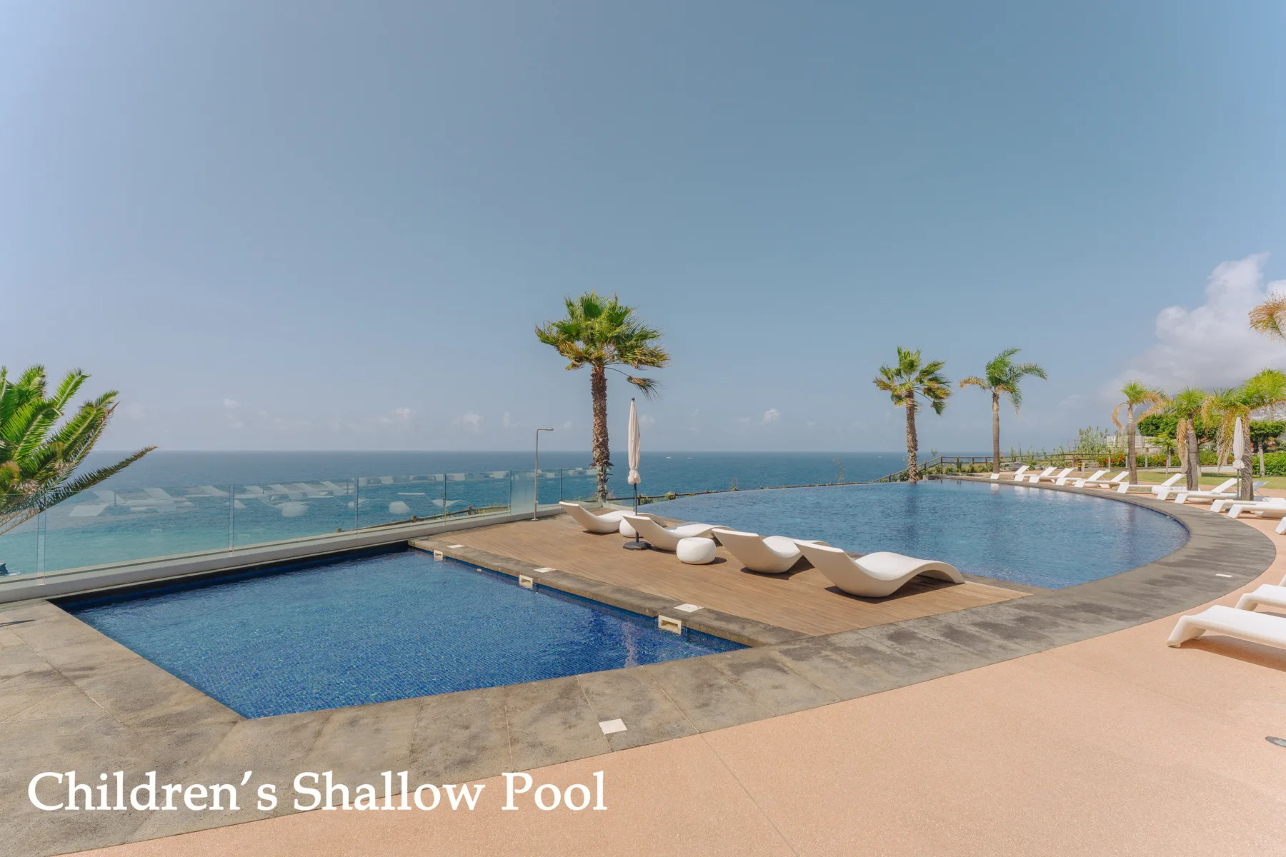 A shallow pool and a larger pool overlook the ocean, with lounge seating beside them.