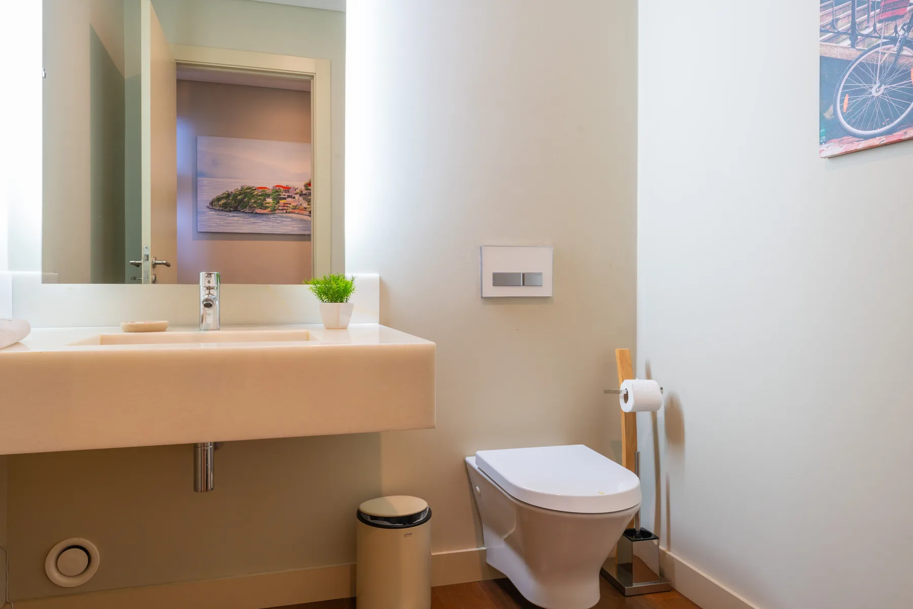 A bathroom with a wall-mounted sink, toilet, and framed artwork.