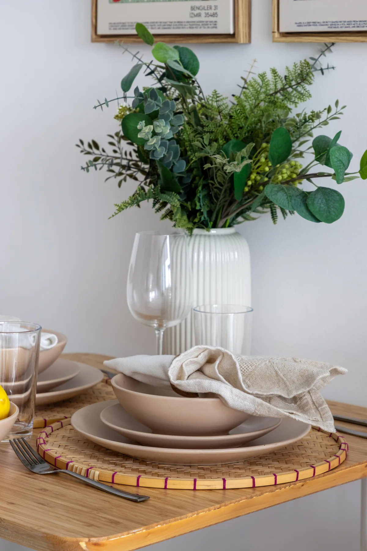 Una mesa de comedor está puesta con vajilla neutra y un jarrón con follaje.